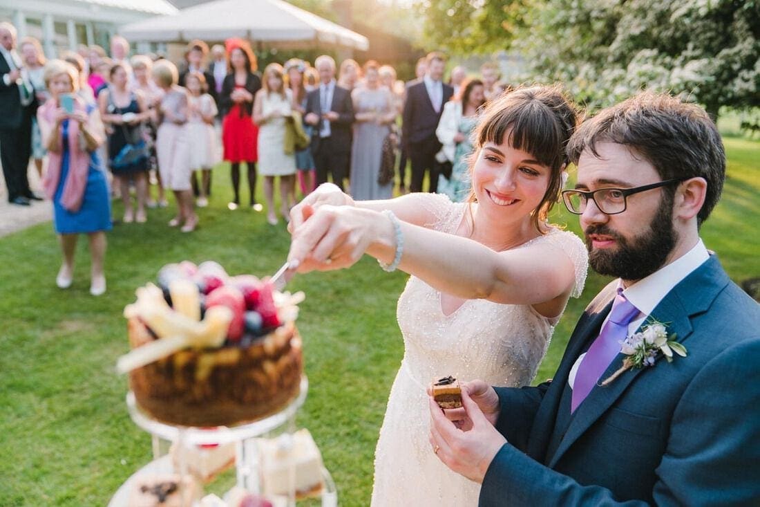 cutting the cake at their outdoor wedding in the sunshine