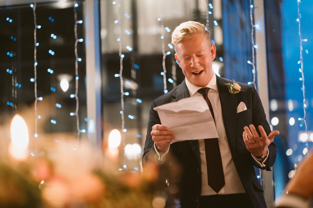 best man gives his wedding speeches with fairy lights in the background